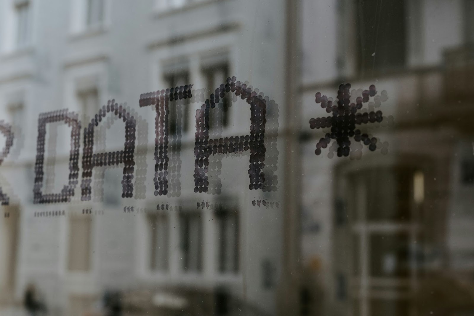 The word "DATA" written in a dot-matrix style on a glass window, with a blurred urban building reflected in the background — illustrating the concept of CRM data quality and HubSpot duplicate management.